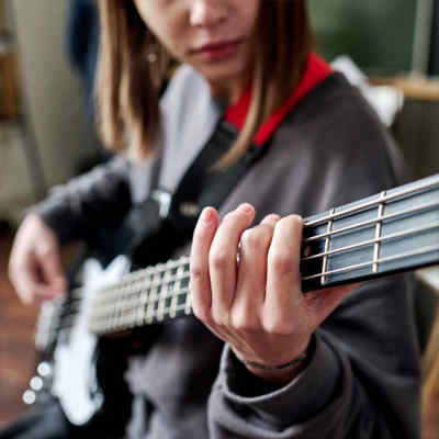 Bass lessons. Close up of girl playing bass. The view is from the head of the bass with the strumming hand in the background.
