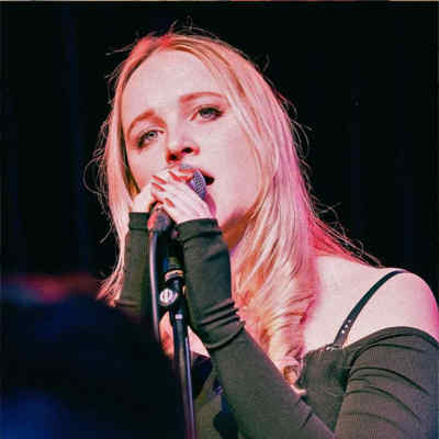 Singing Lessons. A blonde woman sings into a microphone.